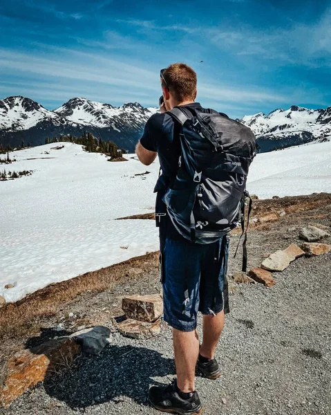 一个带背包的远足男子在惠斯勒布莱克科姆拍照的垂直背影 — 图库照片