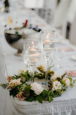 Bir düğün masasında cam mum tutacakları ve çiçeklerin dikey çekimi.