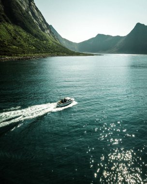 Kuzey Norveç 'te arka planda, denizde ve dağda seyreden bir motorlu botun dikey görüntüsü.