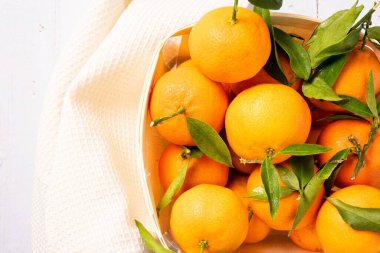 Tabaktaki taze ve sulu mandalinalar ve masada beyaz bir havlu.