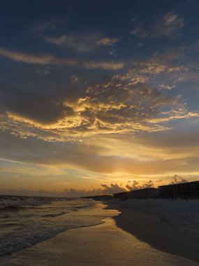 Florida 'nın köpüklü denizi ve kumlu plajı üzerindeki renkli günbatımı bulutlarının nefes kesici manzarası