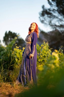 Geleneksel mavi elbisesi ile tarlada altın işlemelerle süslenmiş kızıl saçlı güzel bir bayan.