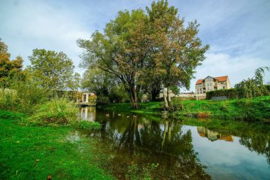 Besancon, Fransa 'da yeşil ağaç ve evleri yansıtan bir göl manzarası