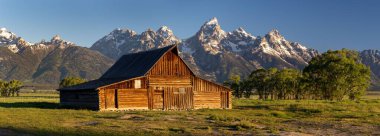 Eski ahşap bir asistanın panoramik görüntüsü. Moose, Wyoming 'deki dağlara karşı yeşil bir arazide Moulton Barn.