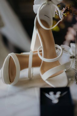 Masadaki beyaz gelinlik ayakkabılarının dikey yakın çekimi.