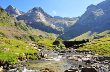 Güneşli bir günde dağlardaki yeşil bir vadiden akan bir nehrin manzarası.
