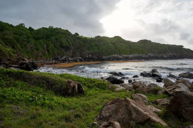 Yeşil uçurumları olan kayalık bir sahil kenarında güzel bir mavi deniz suyu görüntüsü.