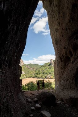 Güneşli bir günde arka planında yeşil tepeler olan bir mağaranın dikey görüntüsü.