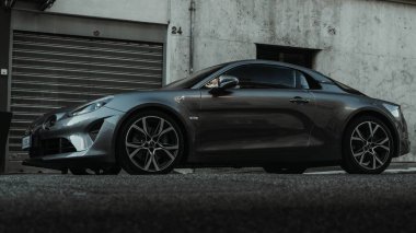 Sakin bir caddeye park edilmiş gri bir Alp 110 spor arabasının alçak açılı görüntüsü.