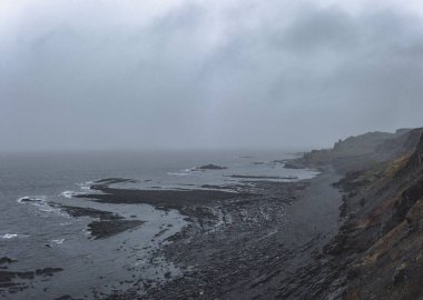 Ufukta sisli bulutlu gökyüzü olan deniz kıyısında kayalık bir uçurum kanyonu