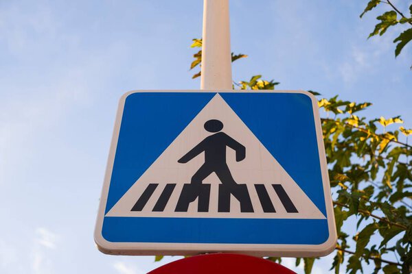The pedestrian crosswalk sign against the blue sky with clouds