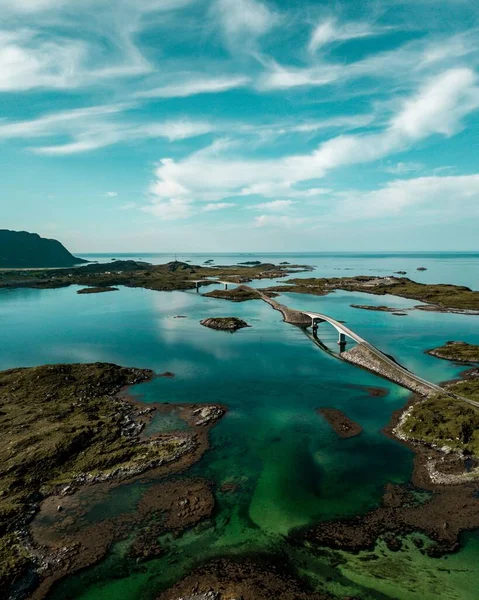 ノルウェー北部の青い曇った空の下で岩の多い海岸の橋の垂直ショット — ストック写真