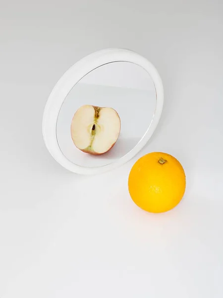 Stock image A vertical shot of an orange reflecting in a mirror as a cut red apple