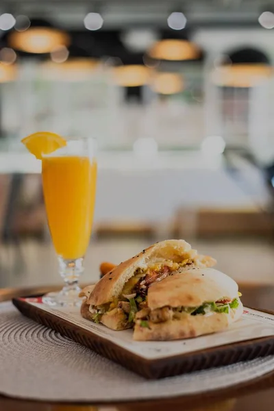 一个垂直的特写镜头 一个切片汉堡和一杯橙汁在餐馆里 模糊的背景 — 图库照片