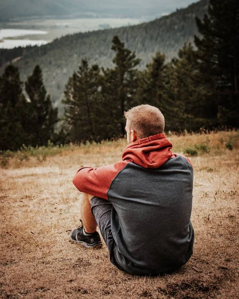 山地男子坐在山坡上的田野上的一个远足男子的竖向照片 — 图库照片