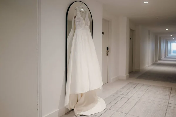 The white bridal dress hanging on the mirror on the wall