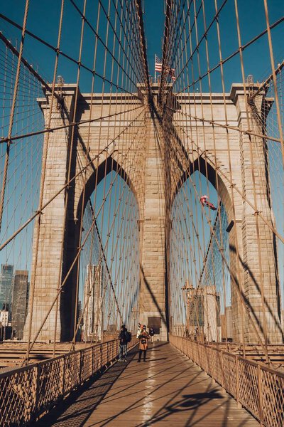 A vertical shot of the Brooklyn Bridge in New York City on a bright, sunny day