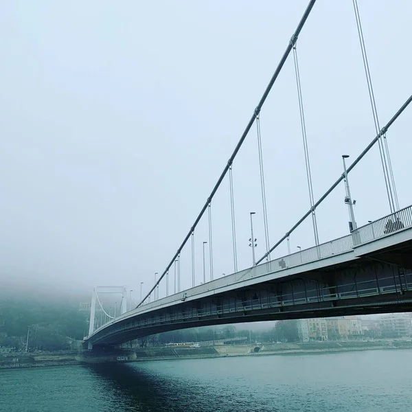 Malownicze Niskokątne Ujęcie Mostu Nad Spokojną Rzeką Mglisty Dzień — Zdjęcie stockowe
