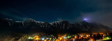 Geceleri dağların eteklerinde aydınlatılmış bir kasabanın panoramik görüntüsü.