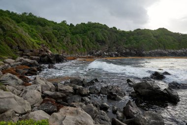 Yeşil uçurumları olan kayalık bir sahil kenarında güzel bir mavi deniz suyu görüntüsü.