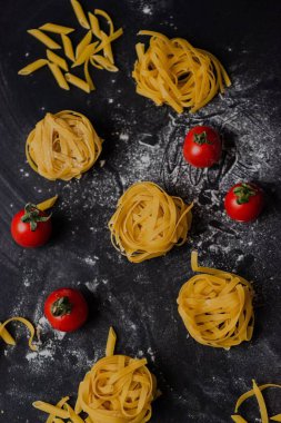 Güzel dekore edilmiş domatesli, siyah arkaplanlı bir makarnanın dikey yakın çekimi.