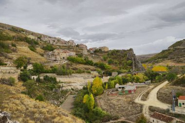 Sarı ve yeşil ağaçlı bir yamaçtaki dağınık evlerin hava manzarası.