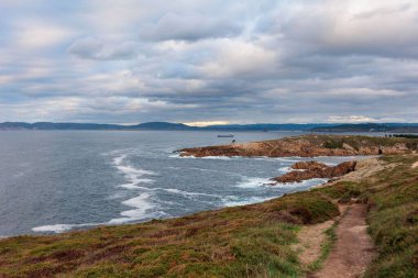 Kasvetli bir günde rüzgarlı bir denizde yüksek açılı bir manzara ve etrafında sarı otlar, Galiçya, İspanya