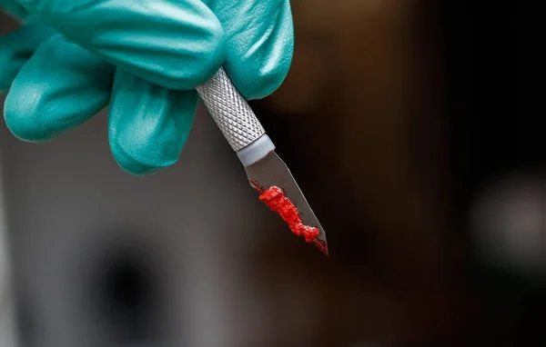 stock image A hand in a green plastic glove holding a scalpel covered in blood