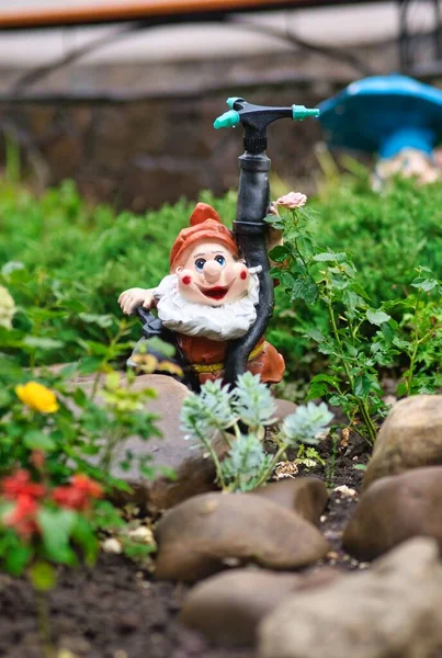 一个红帽花园侏儒的垂直镜头 放置在一个洒水装置旁边 — 图库照片