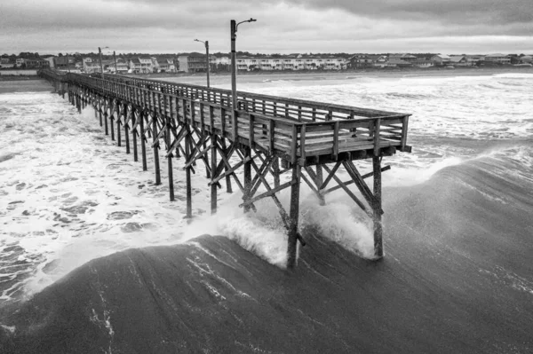 グレースケールで撮影されたビーチに対してクラッシュ海の波に木製の桟橋の高角度ショット — ストック写真