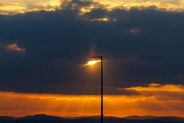 Een Silhouet Van Een Lantaarnpaal Onder Een Heldere Bewolkte Zonsondergang — Stockfoto