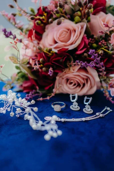 結婚式の宝石類の垂直クローズアップショットと青いテーブルの上にバラの花束 — ストック写真