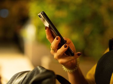 Genç bir bayanın elindeki cep telefonunun yakın plan görüntüsü.