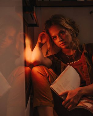 Düşük çözünürlüklü bir ışıkta mutfakta oturan sarışın bir kadının dikey görüntüsü.