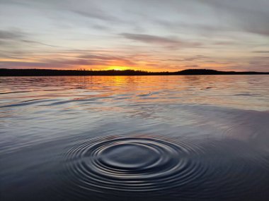 Suda bir dalgalanma ve arka planda bir günbatımı