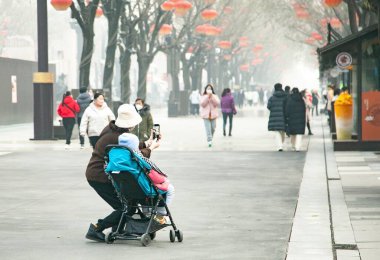 Çocuğuyla birlikte bebek arabasının yanında duran ve bir caddenin fotoğraflarını çeken genç bir anne.