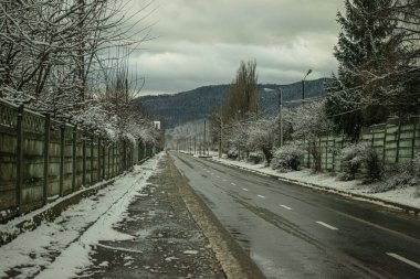 Kışın ıslak bir yol, etrafta kar ve kasvetli bir arka plan.