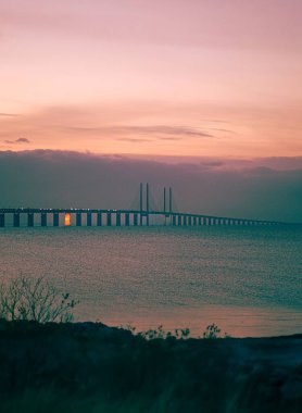 Güzel Öresund Köprüsü 'nün arka planda pembe günbatımı olan dikey bir görüntüsü.