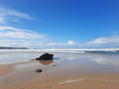 Bulutlu mavi gökyüzünün altındaki kumsalda güzel bir kaya görüntüsü.