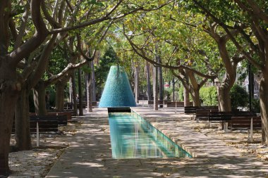 Çeşmeli küçük bir su kütlesinin her iki tarafında ağaçlar var..