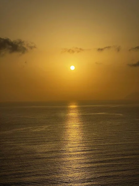 A vertical shot of the golden sunset shining above the calm sea with the horizon in the background