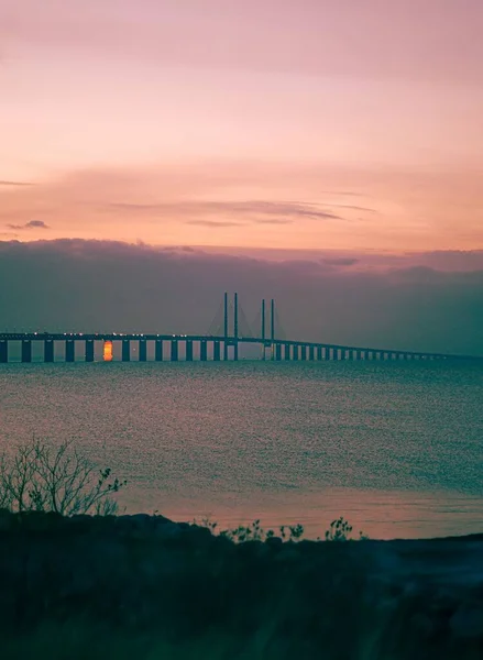 背景にピンクの夕日と海の上の美しいオレンジ色の橋の垂直ショット — ストック写真