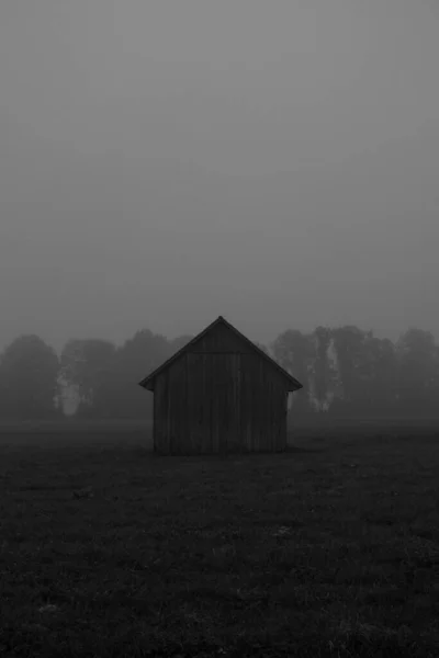 グレースケールで撮影霧の日にフィールド内の木造小屋の垂直 — ストック写真