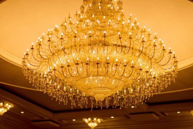 Tavanda asılı lüks bir avizenin düşük açılı bir görüntüsü. Bir sürü ampul açık, camsı süslemelerle süslenmiş.