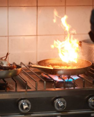 Ocakta yemek pişiren alevli bir tavanın dikey görüntüsü.