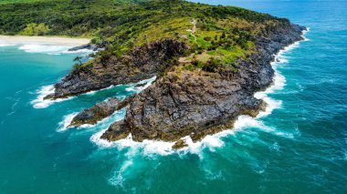 Deniz dalgalarının kayalık ve yeşillik plajları kırdığı bir hava manzarası.