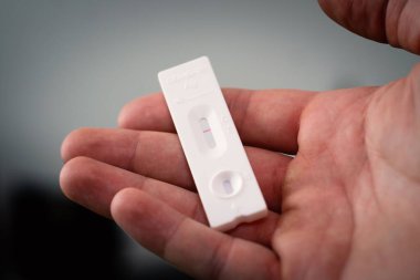 Hızlı bir covid-19 testi tutan bir elin seçici odak noktası beyaz bir tabloda negatif sonuç verir.