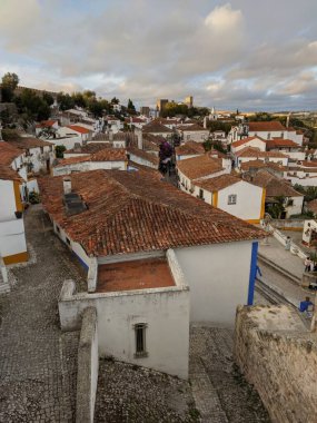 Bulutlu bir gökyüzünün altında tuğladan kırmızı çatıları olan Obidos kasabası.