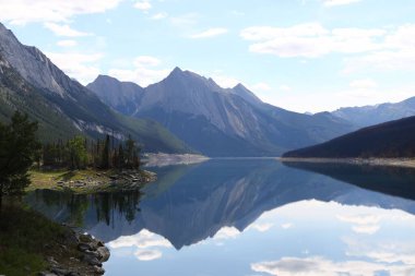 Huzurlu bir göl manzarası dağları ve kıyılarındaki yeşil ağaçları yansıtıyor.