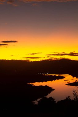 Gün batımında tepelerin silueti ve bir nehir.